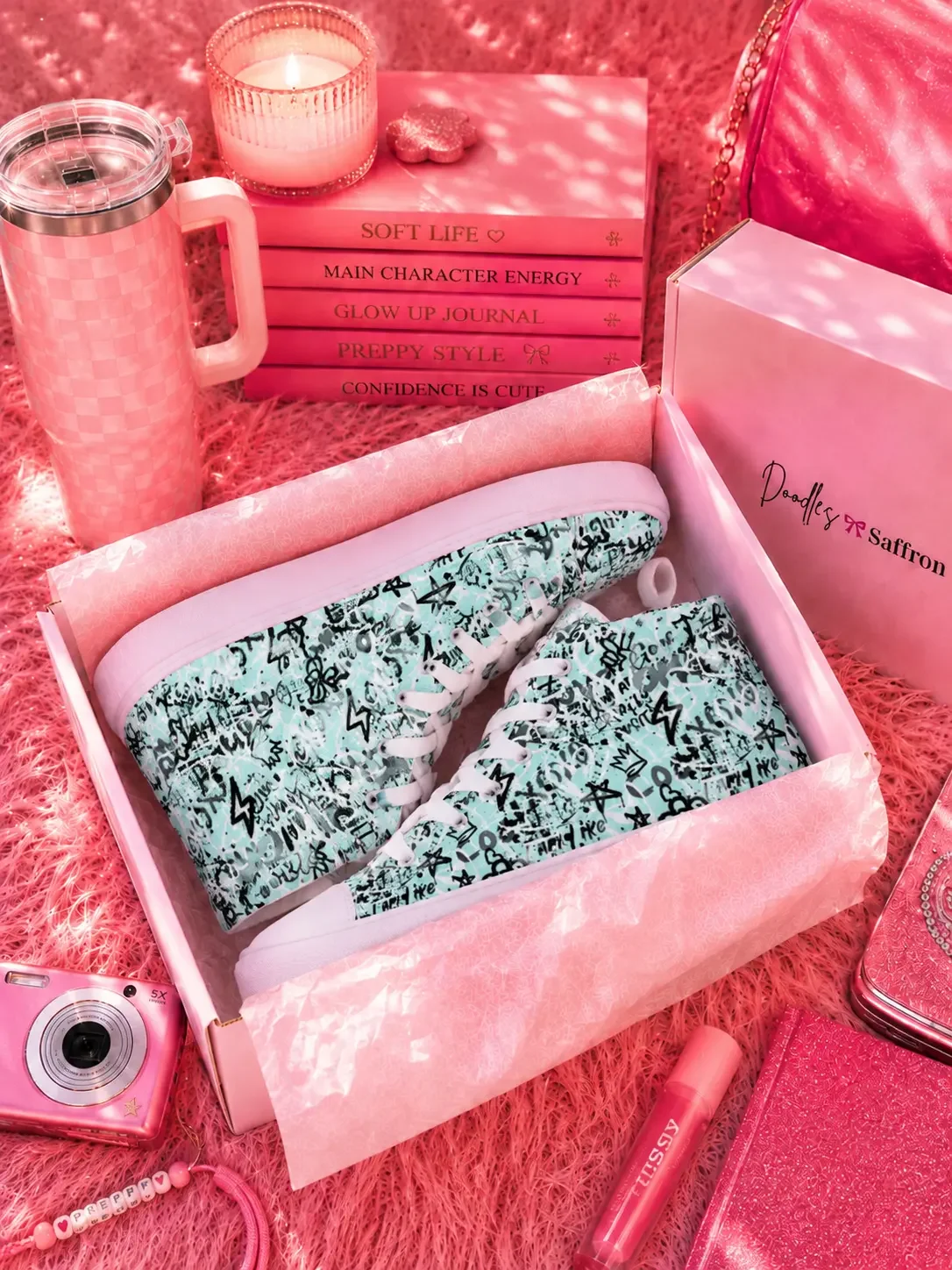 A pair of mint green graffiti print high-top sneakers packed neatly inside an open white Doodles and Saffron shoebox on a pink shag rug.