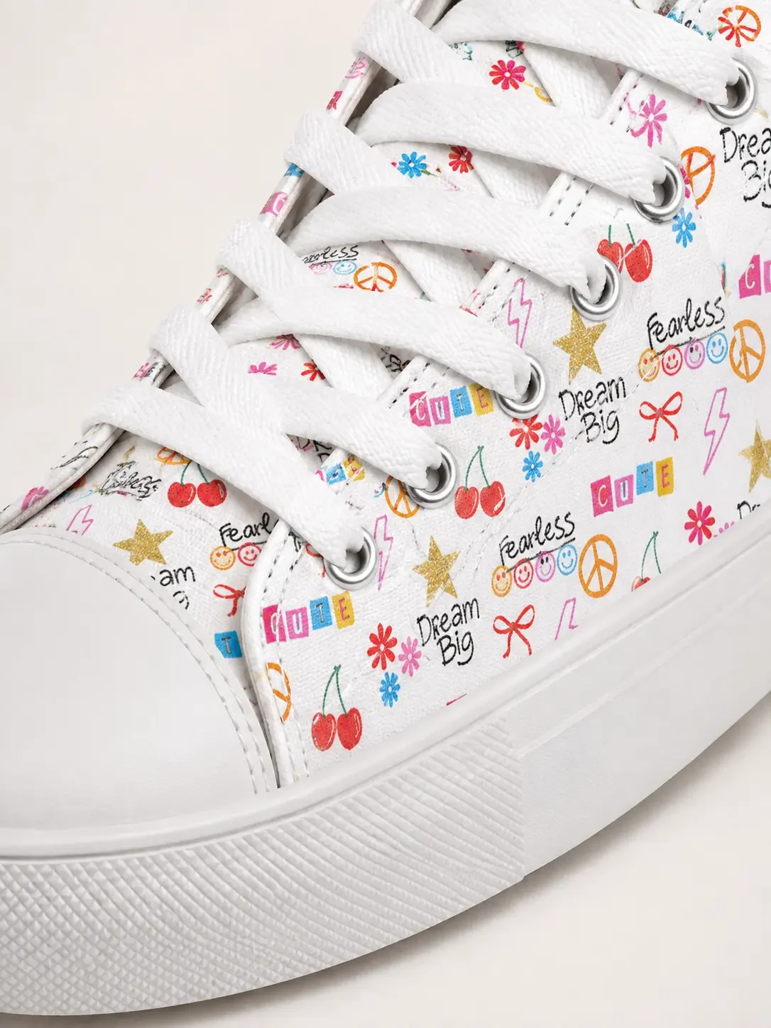 Close-up of a white canvas sneaker featuring a colorful graphic pattern of cherries, peace signs, stars, and text.