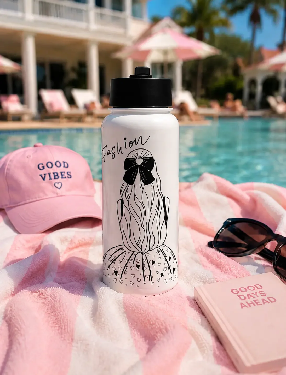 White fashion illustration water bottle sitting on a pink striped towel by a sunny luxury resort swimming pool.