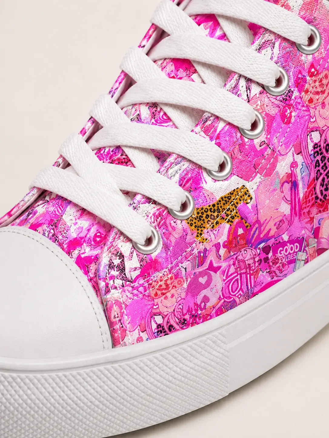 Close-up detail of white laces, rubber sole, and a vibrant pink canvas material featuring a street art graffiti pattern.