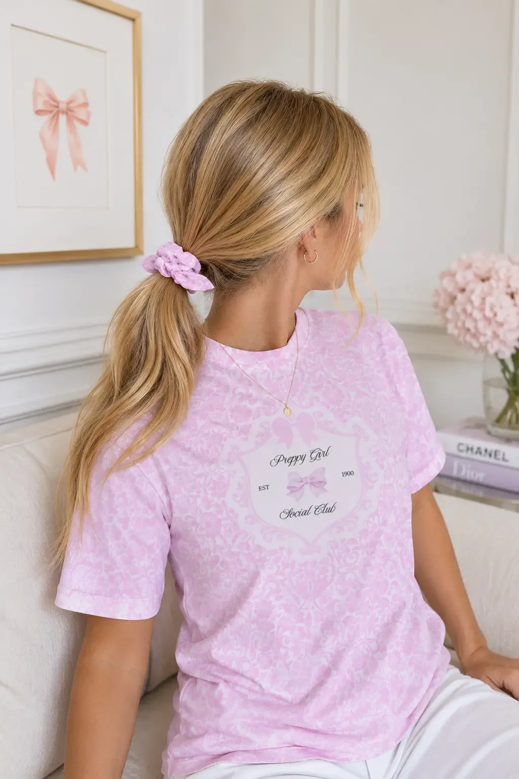 Profile of a blonde woman on a white sofa wearing a pink scrunchie in a low ponytail and a matching graphic t-shirt.