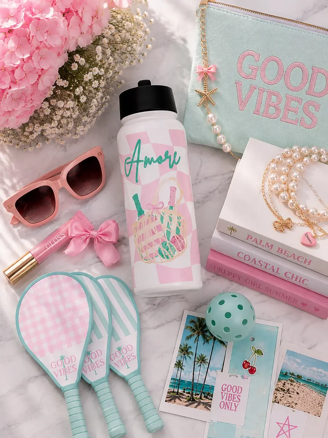 A white Amore print water bottle next to a pink sports duffel bag, pickleball paddle, and heart sunglasses.