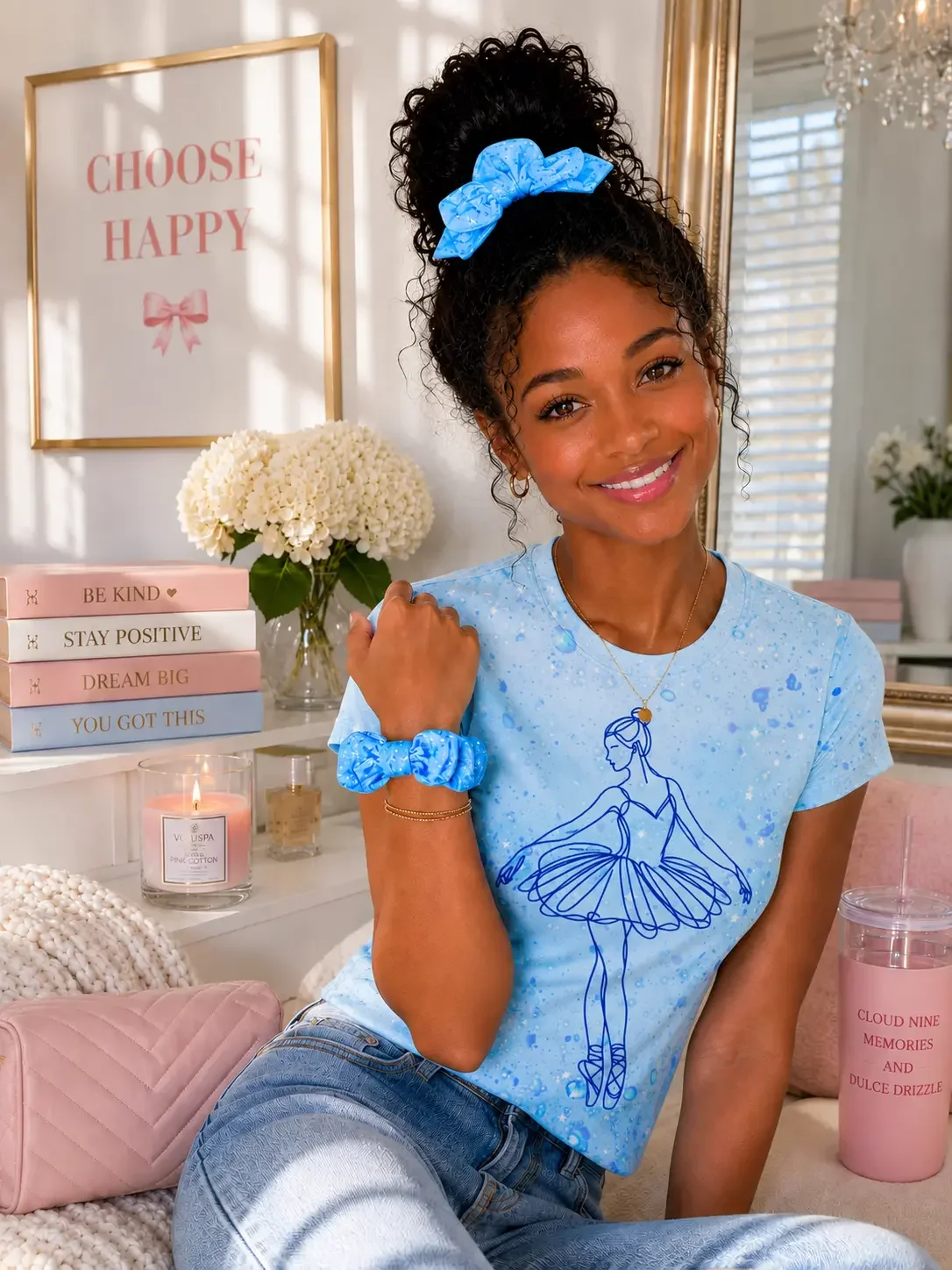 Smiling woman with a curly hair bun, wearing a blue star bow scrunchie, matching ballerina graphic t-shirt, and wrist scrunchie.