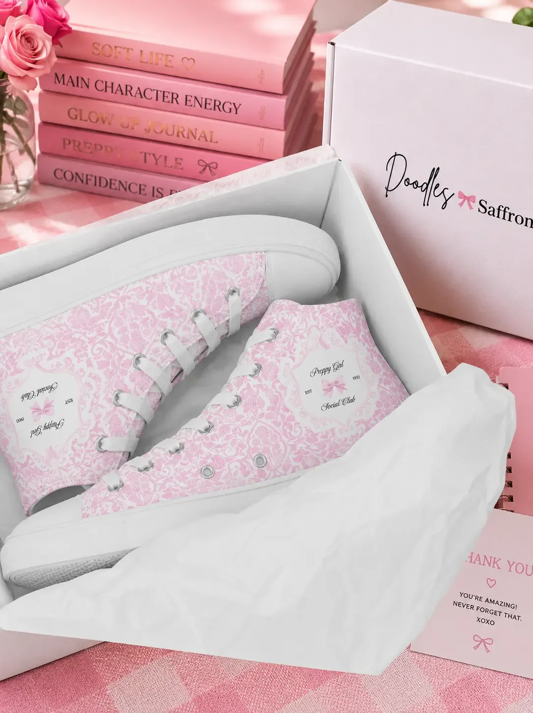 Pink toile print high-top canvas sneakers inside a retail shipping box surrounded by pink preppy aesthetic journals and stationery accessories.