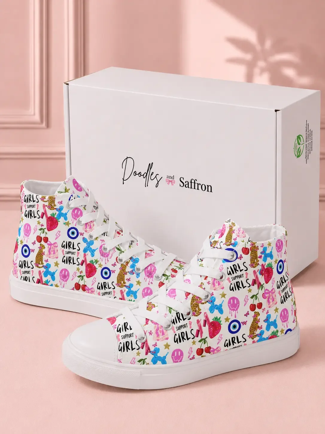 Pair of white graphic high-top canvas sneakers standing in front of a white Doodles and Saffron branded shipping box.