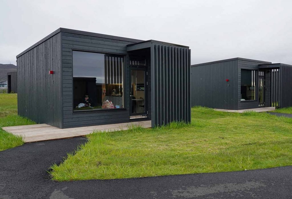Modern black wood cabins with large windows on a grassy landscape.