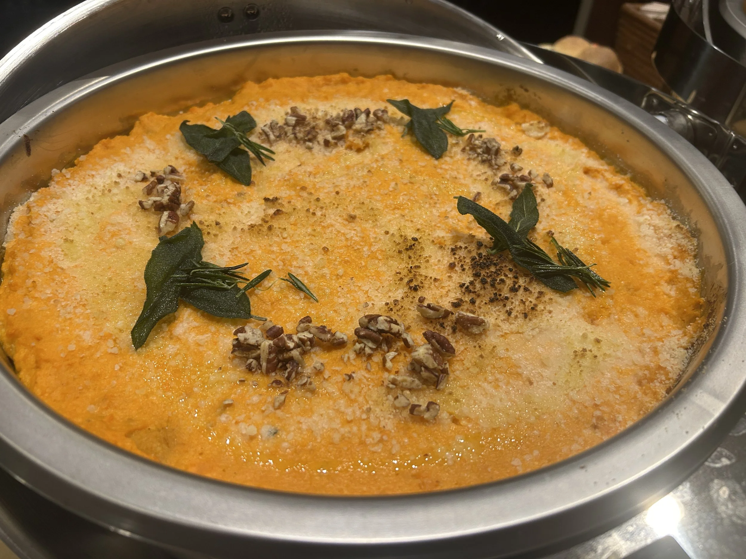 Close-up of a dish in a round metal skillet, topped with chopped herbs, grated cheese, and pepper.