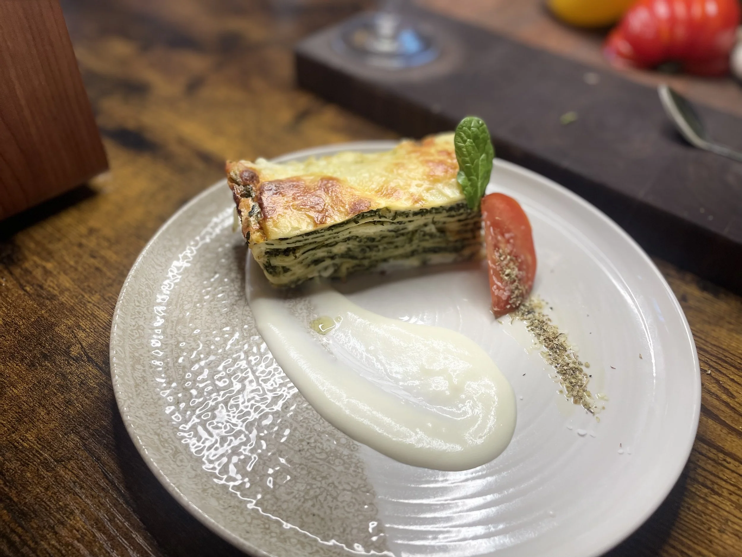 A slice of layered spinach and cheese lasagna on a white plate, garnished with a fresh basil leaf and a cherry tomato, served with a drizzle of creamy white sauce.