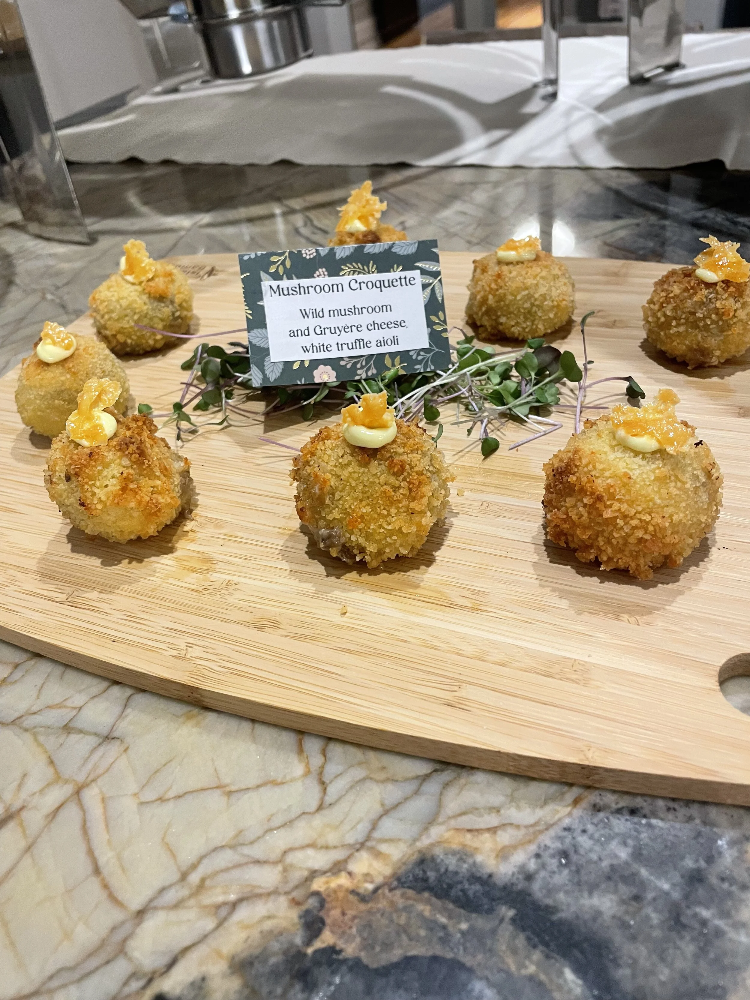 Crispy mushroom croquettes with cheese and truffle aioli, garnished with orange peel and microgreens on a wooden platter.