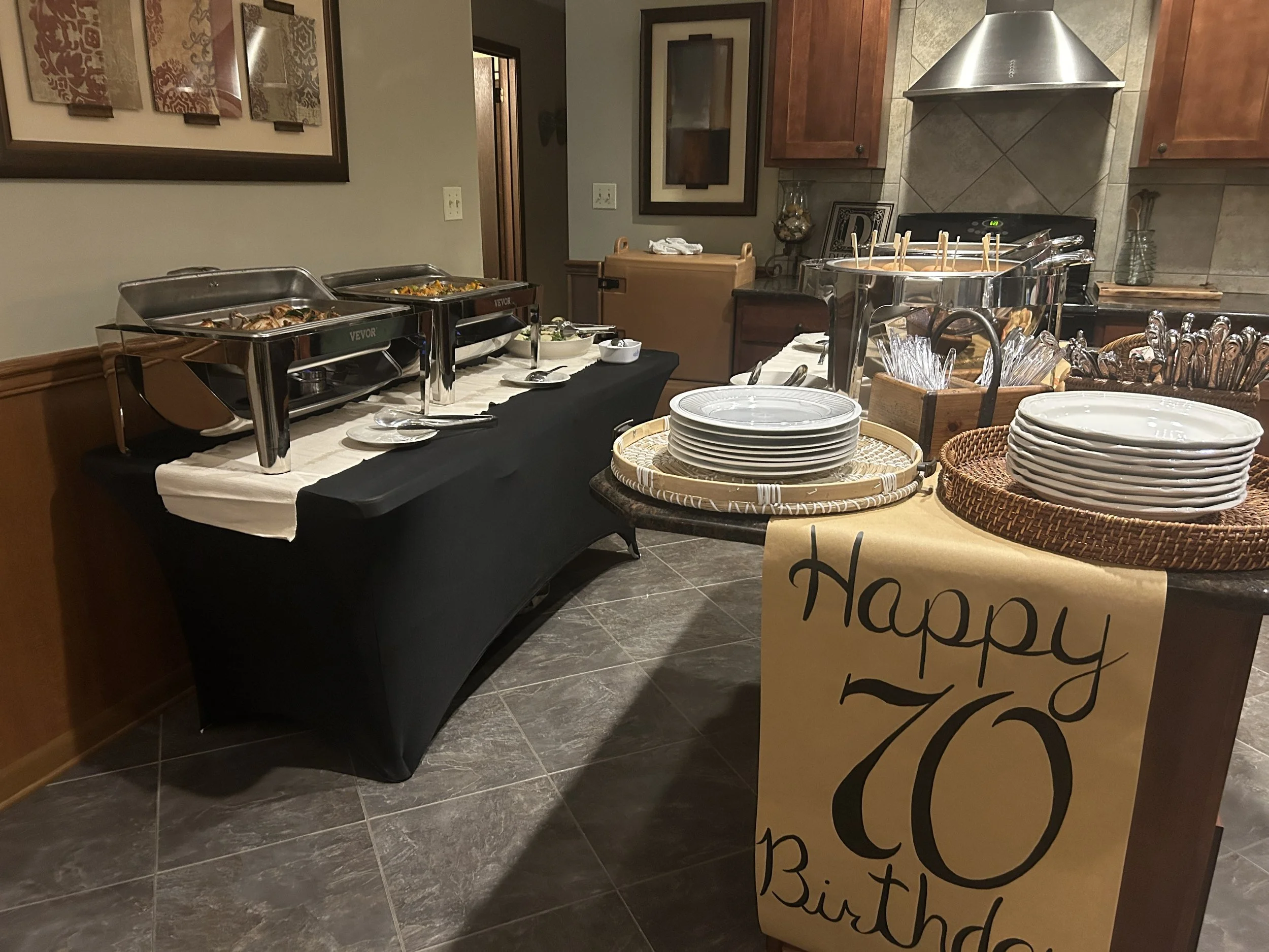 A buffet table with chafing dishes, plates, and serving utensils in a room with framed artwork and decorative wall items.
