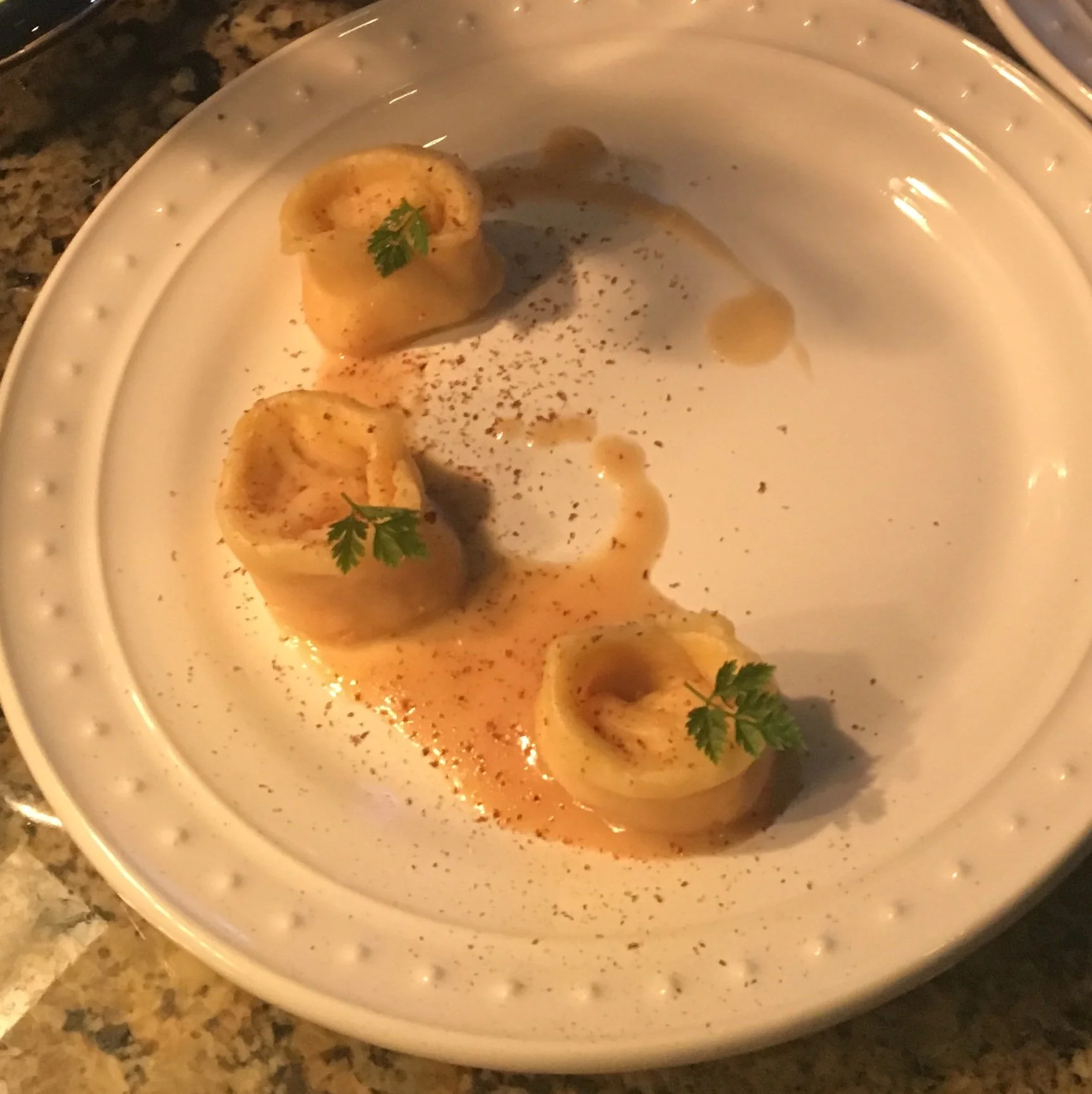 Three stuffed pasta shells on a white plate garnished with parsley, drizzled with sauce, sprinkled with spices.
