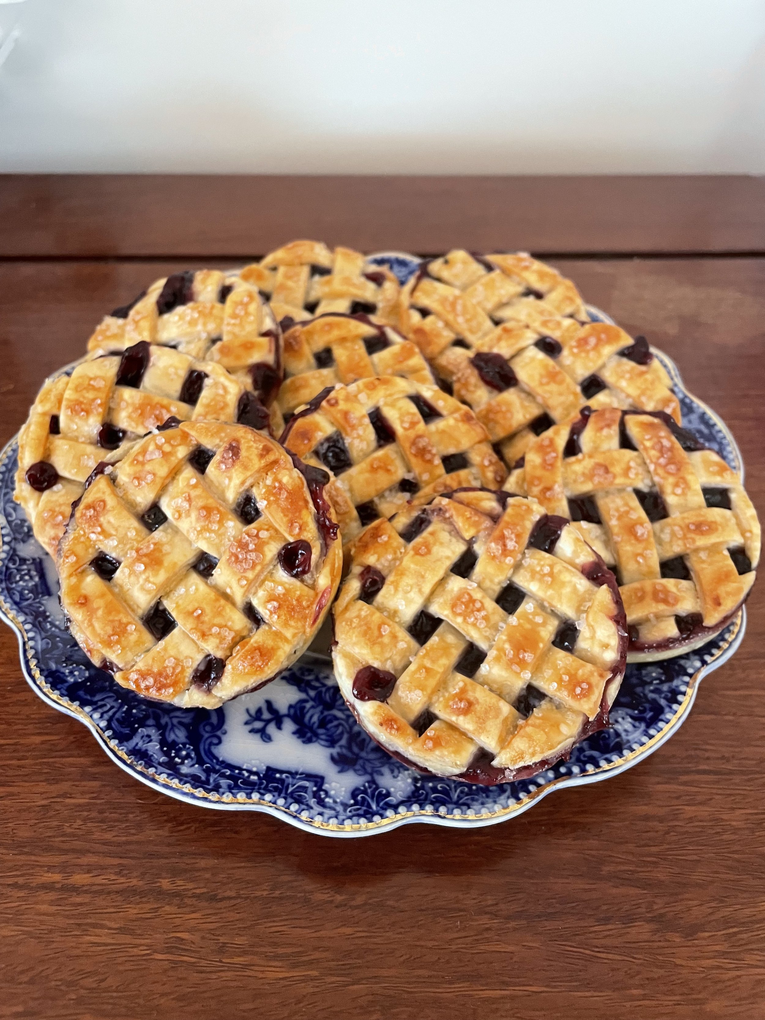 A decorative blue and white plate holding several lattice-topped cherry pies on a wooden table.