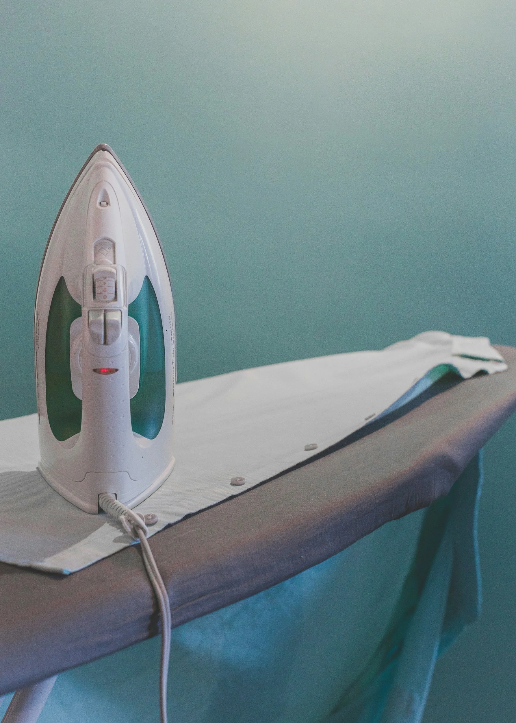 An electric steam iron placed on an ironing board with a blue wall background.