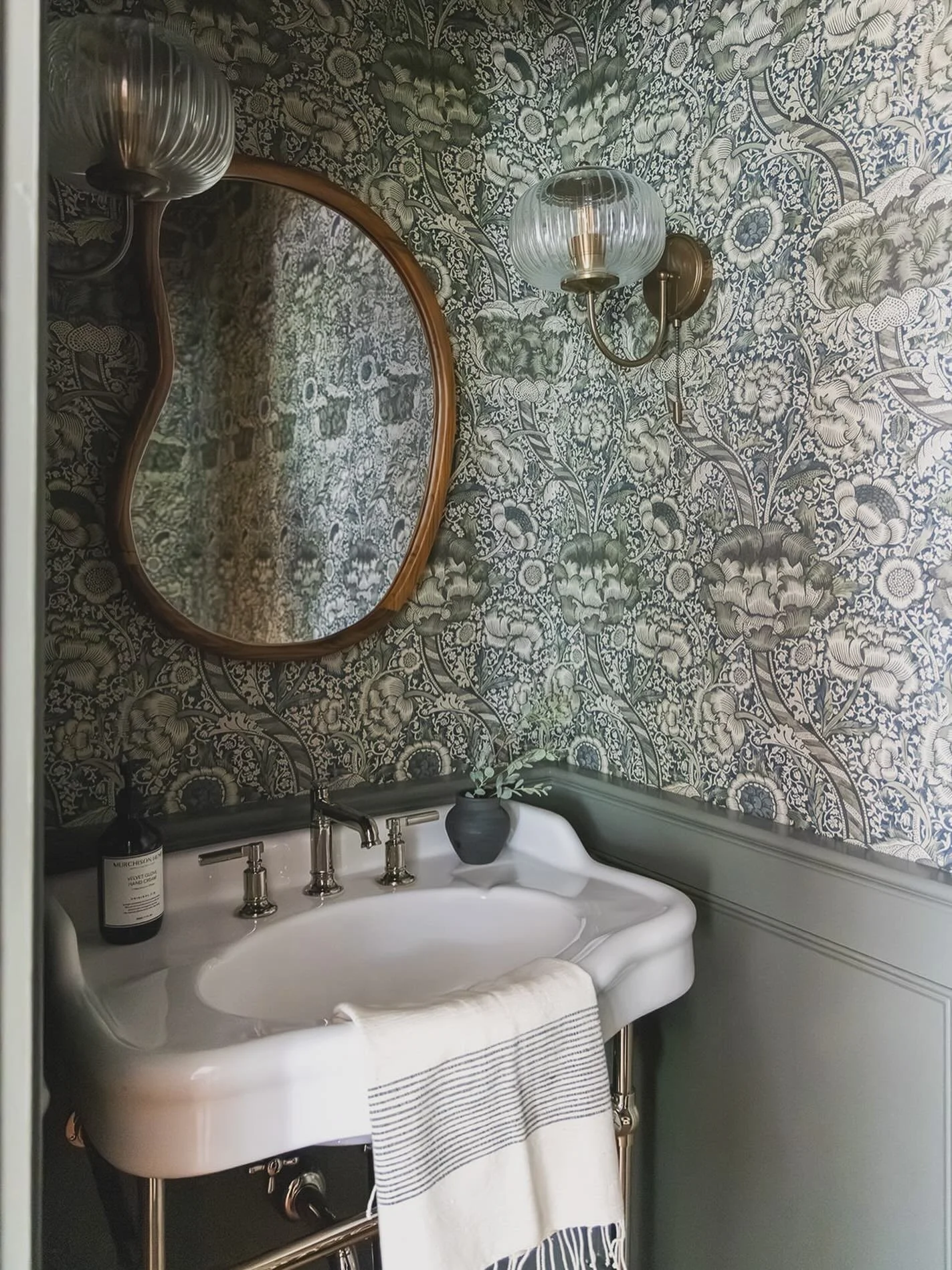 Small space, big personality. This moody powder room layers bold botanical wallpaper, rich wood tones, and vintage-inspired fixtures for a look that&rsquo;s timeless yet full of character #PowderRoomGoals #BoldDesign #ambermarquesinteriors