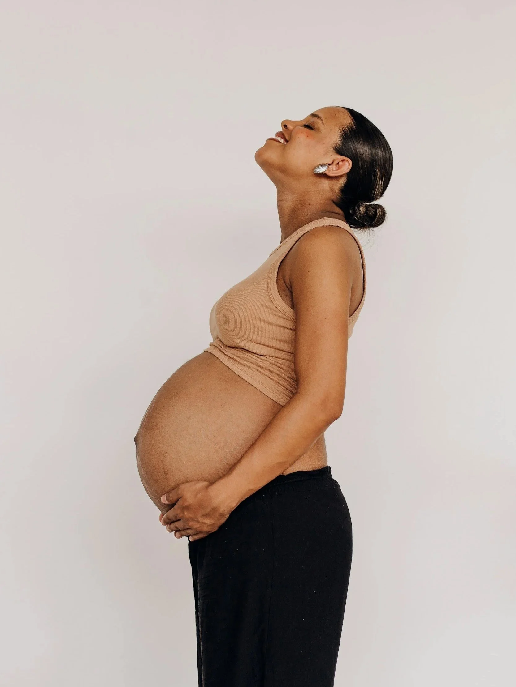 Pregnant woman smiling while holding her belly, representing weight-neutral perinatal nutrition support for the fourth trimester