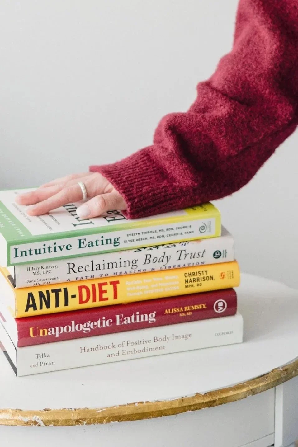 Intuitive eating dietitian Alexis Culhane resting her hand on a stack of Intuitive Eating and Body Trust books