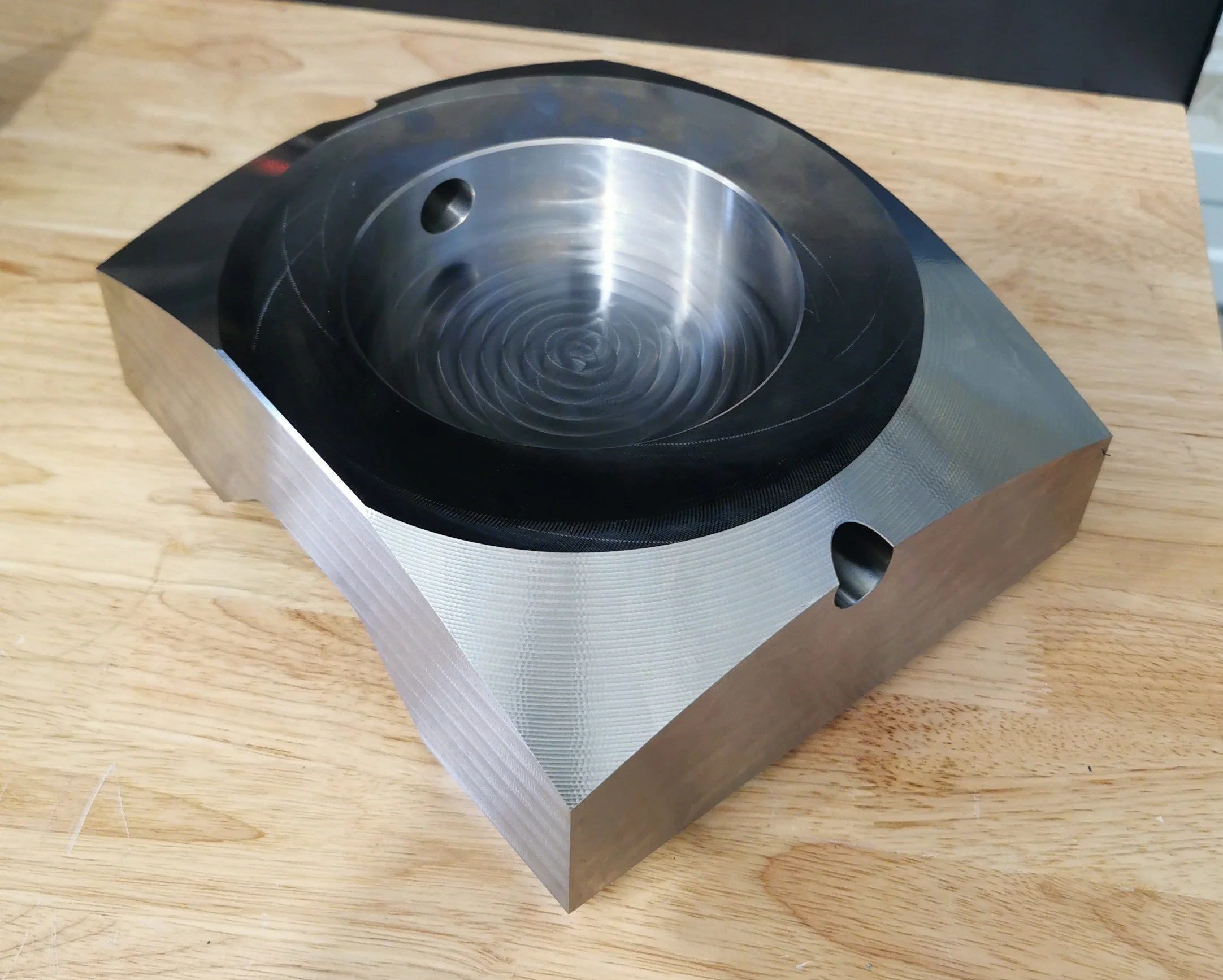 A metallic, rounded, square-shaped object with a circular, black heat-resistant surface on top, placed on a wooden surface.