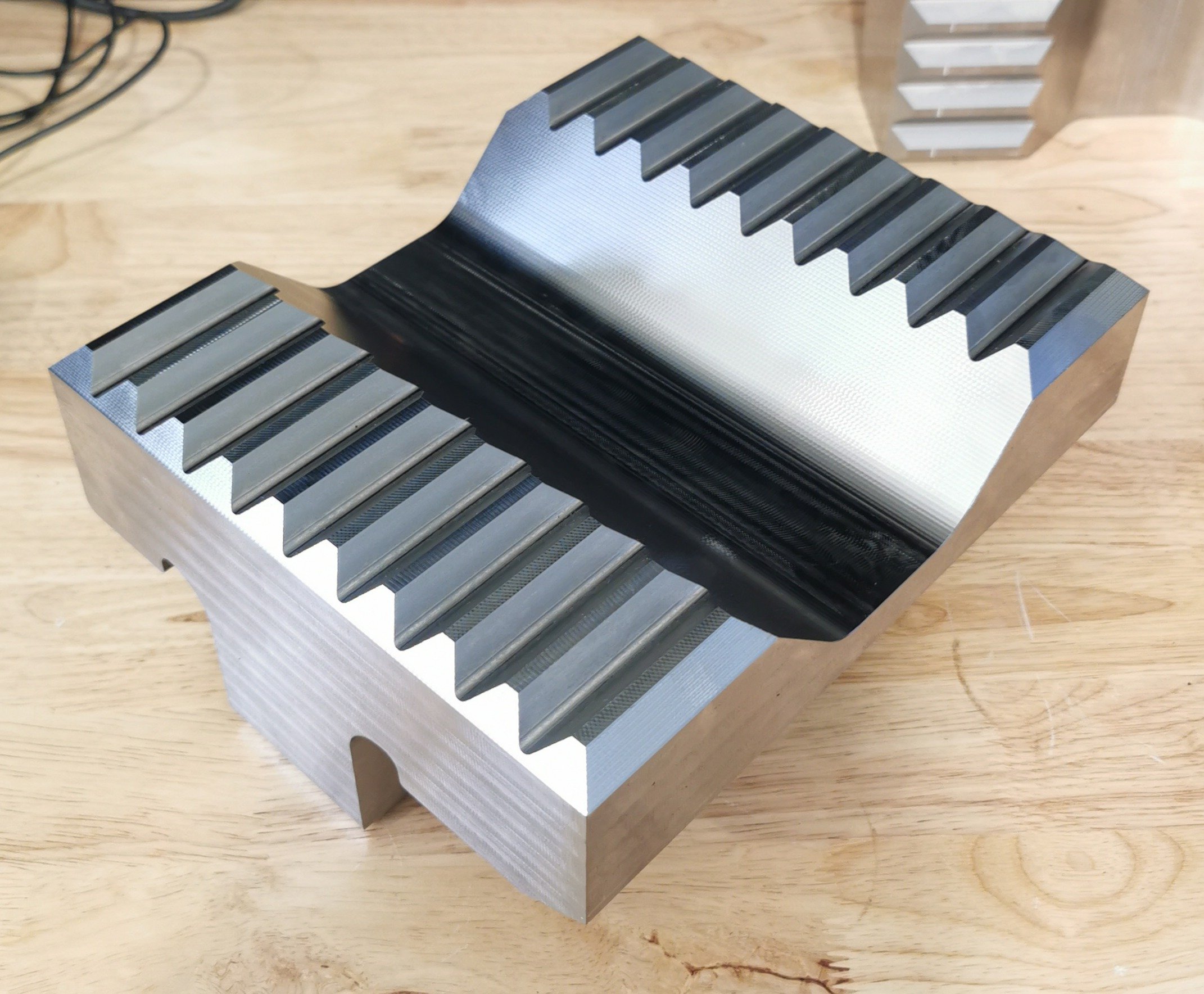 A metallic object with grooves and ridges, placed on a wooden surface. The object has a shiny, reflective finish and appears to be a precision-machined component.