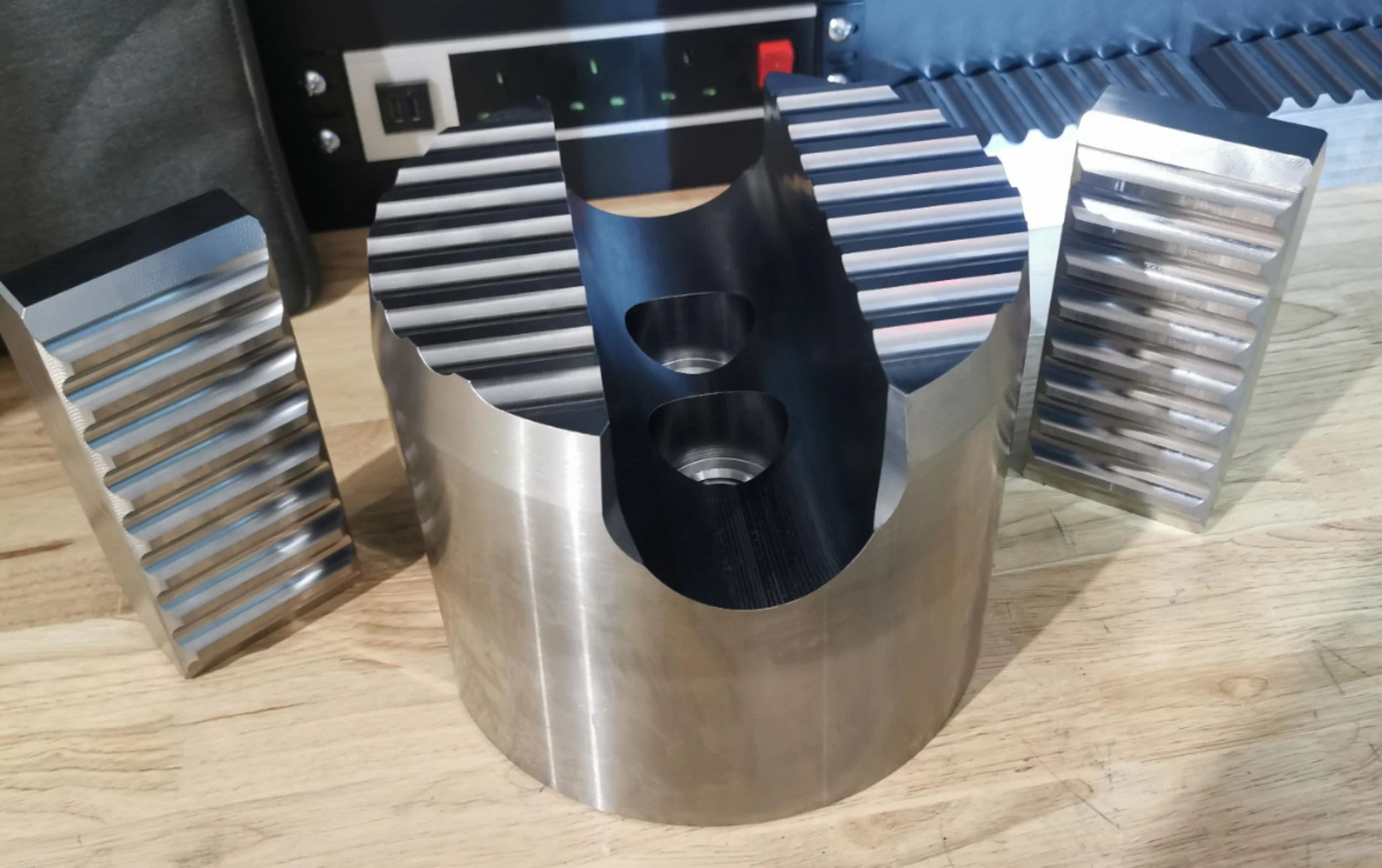 A metallic engine part with fins and two circular holes in the center, placed on a wooden surface.