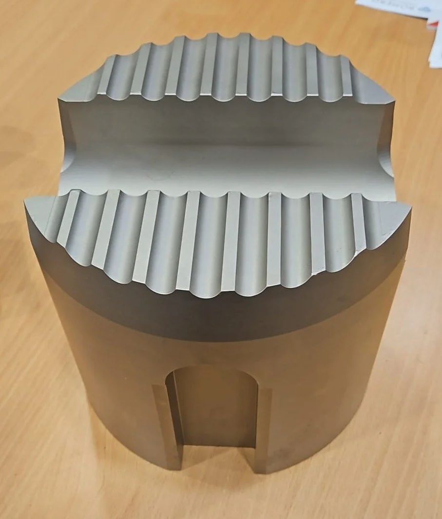 A metallic, cylindrical container with ridged, semi-circular top edges and an open, arch-shaped cutout on the side, placed on a wooden surface.