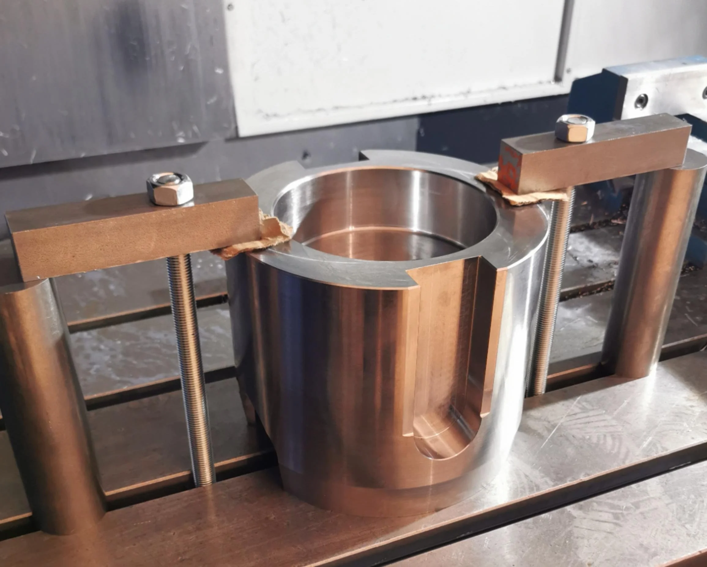 A metal cylindrical component secured with clamps and bolts on a machine worktable.