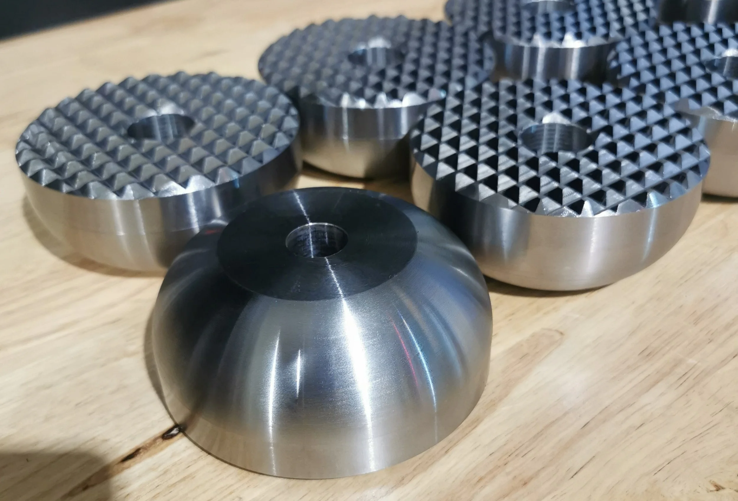 Several metallic foam metal press dies with textured surfaces and smooth sides, placed on a wooden surface.