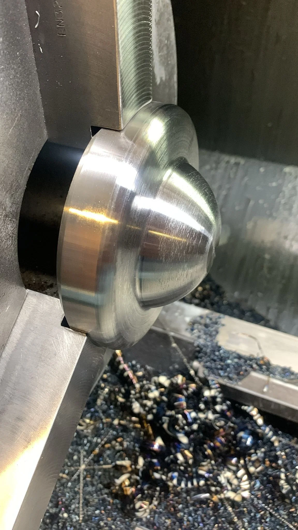 A close-up of a metal grinding or cutting machine in operation, with metal shavings on the work surface.