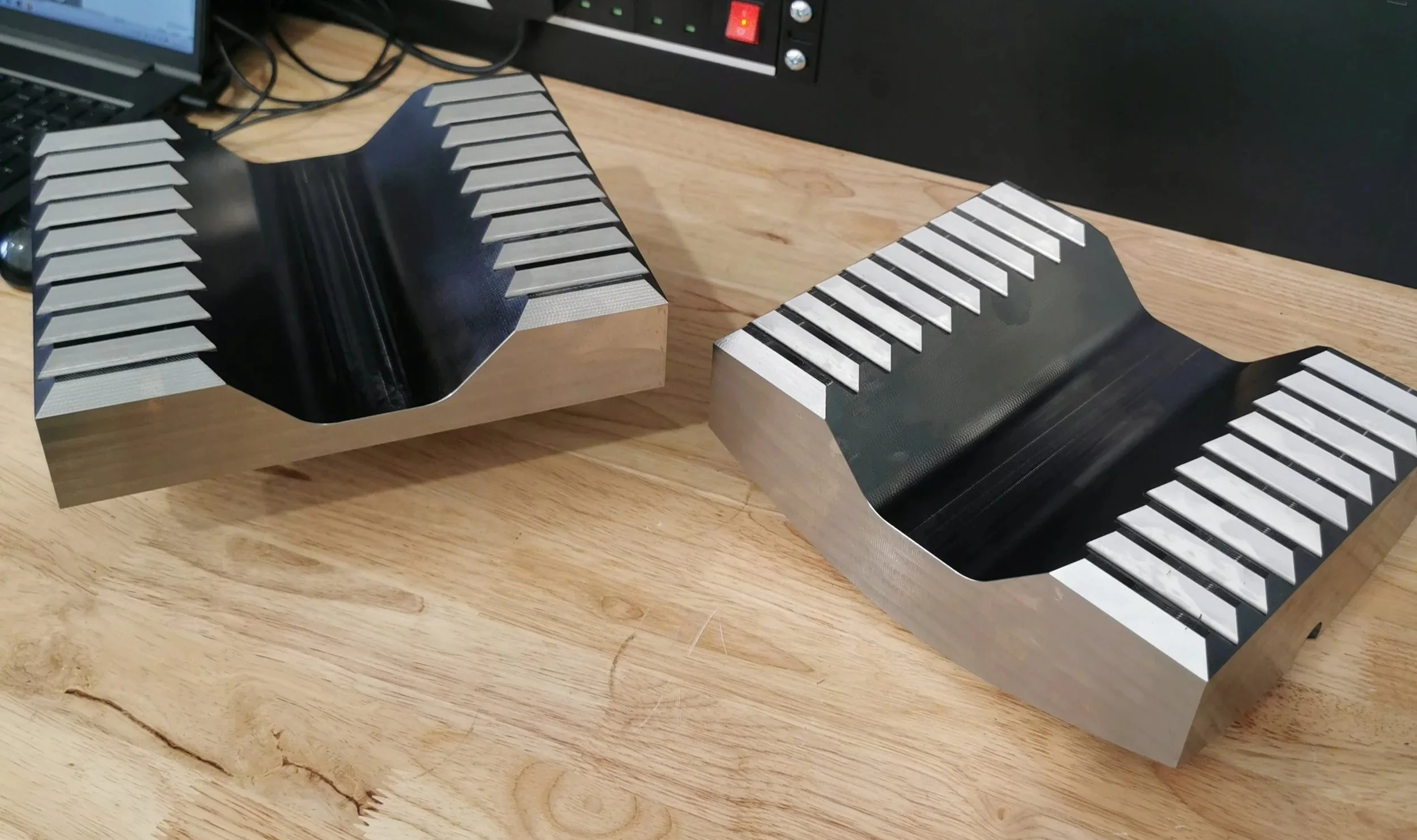 Two precision-machined metal parts with grooved surfaces, placed on a wooden table.