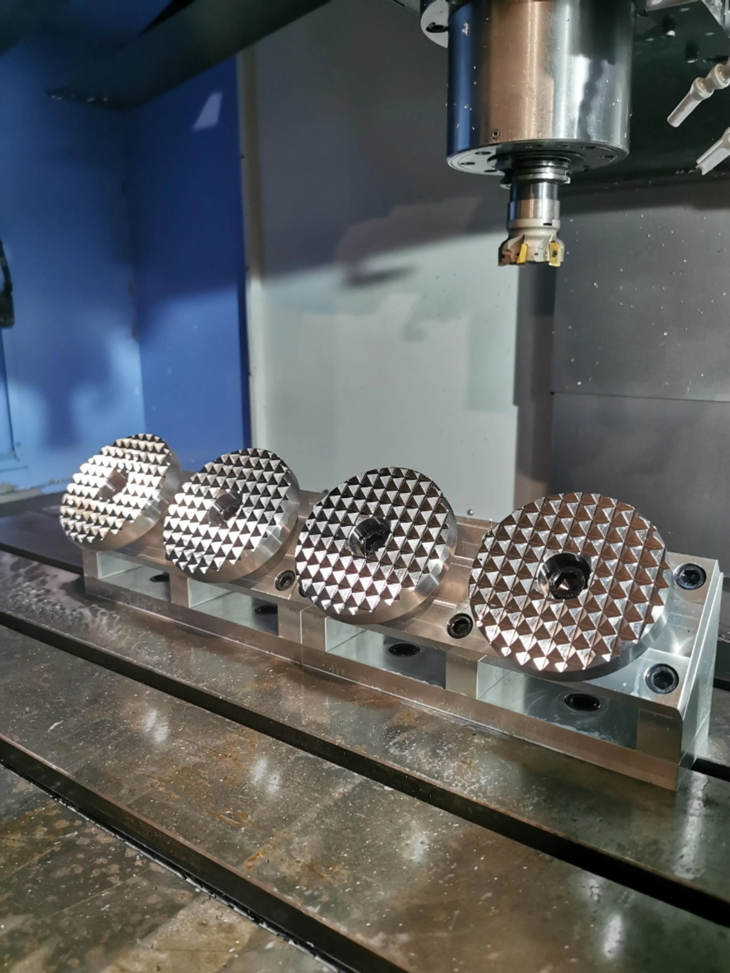 Four metal circular parts with a textured, diamond-patterned surface on a machine tool, likely for manufacturing or machining processes.