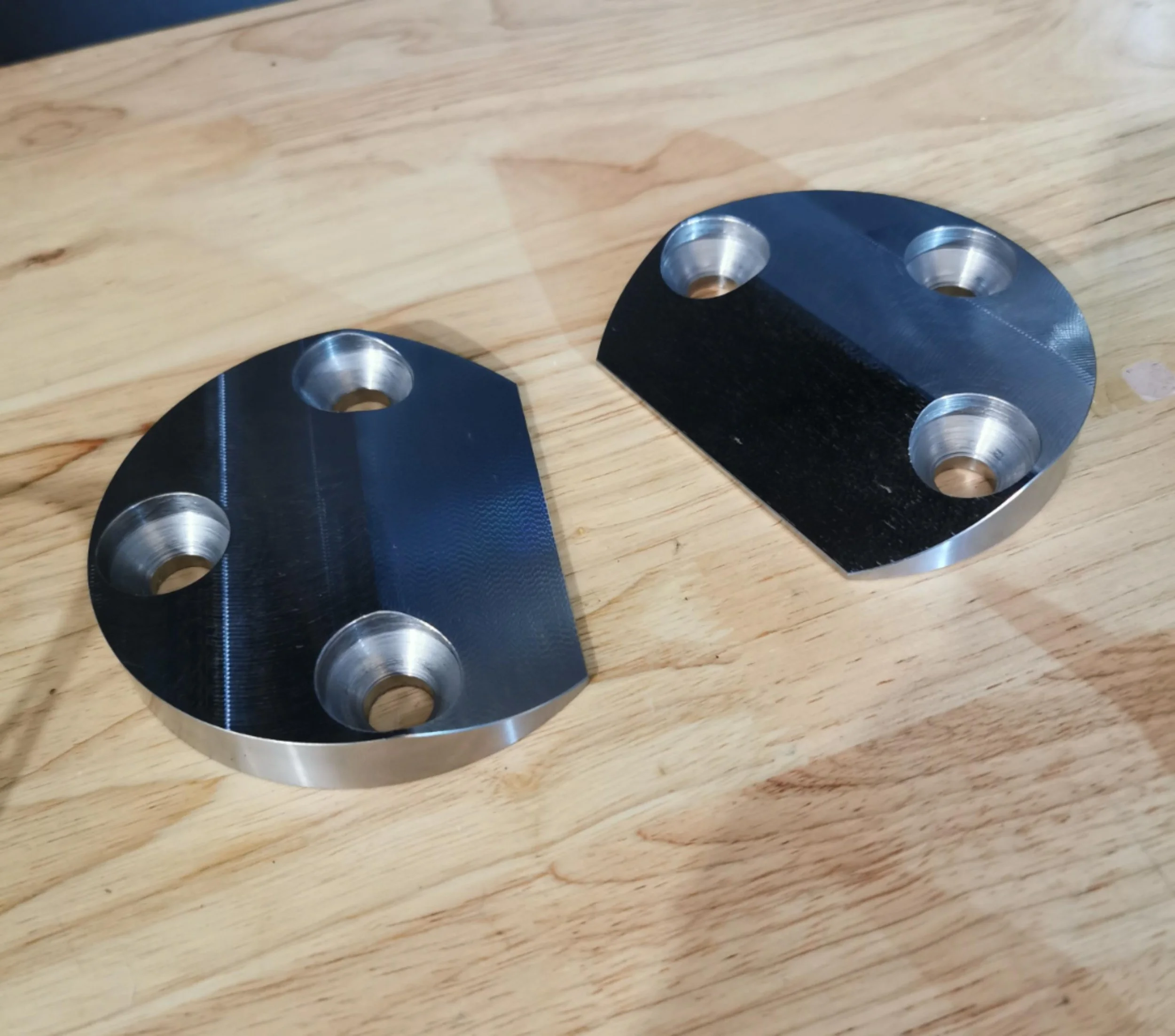 Two black metal brackets with three circular holes each, placed on a wooden surface.