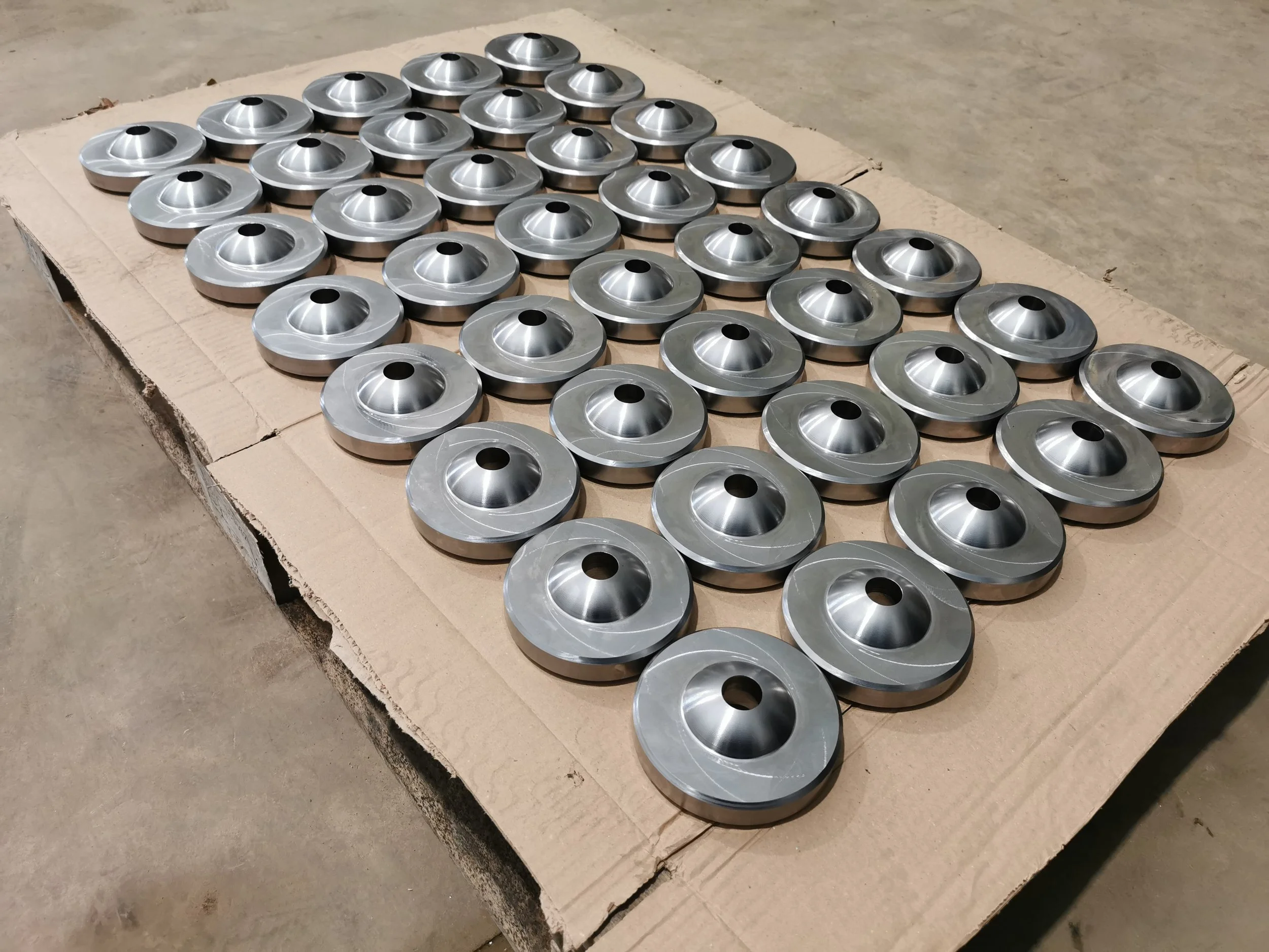 Multiple metallic circular car hubcaps arranged on a cardboard surface in a grid pattern.