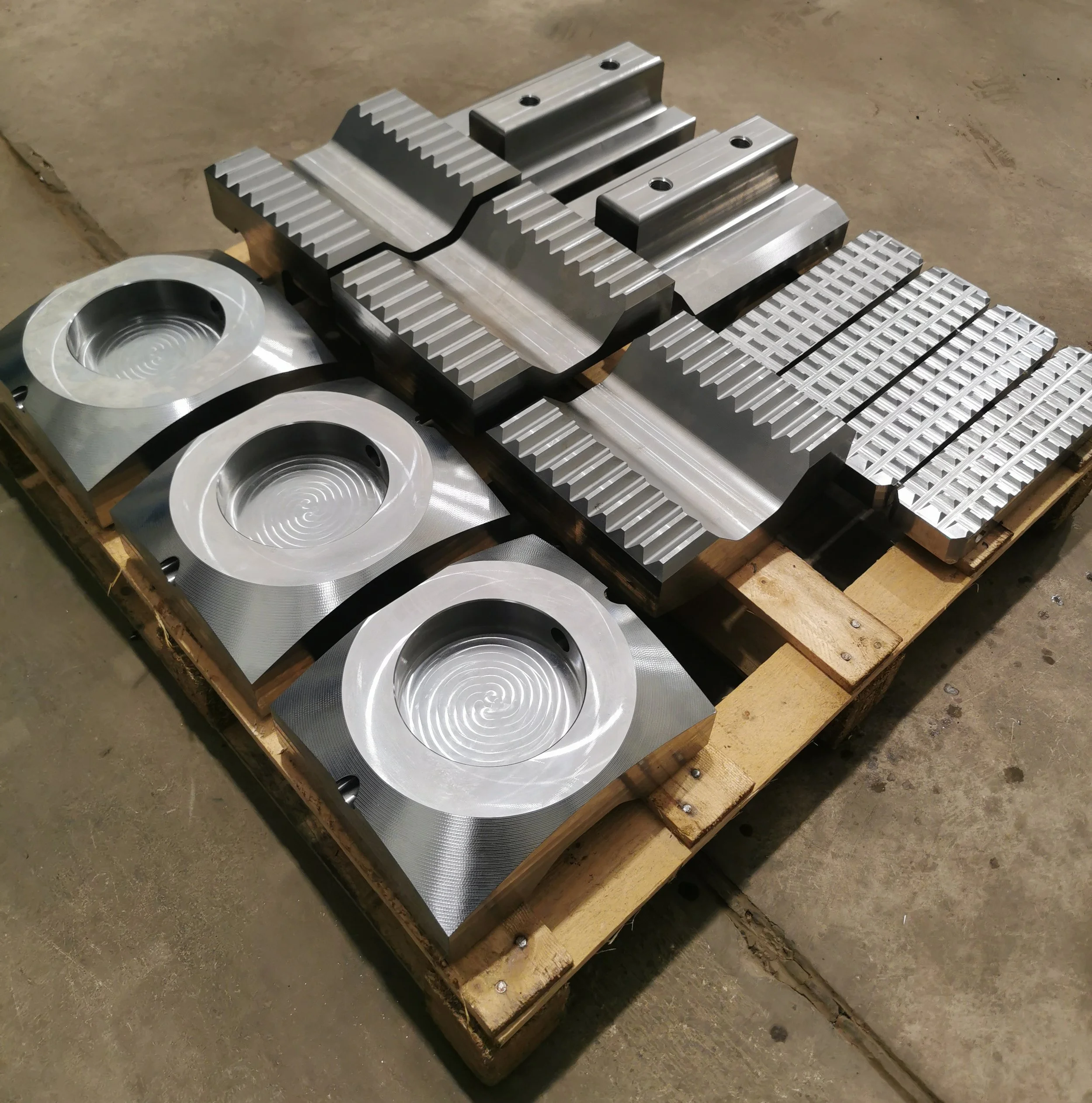 Set of large metal machined parts with grooves, ridges, and circular indentations on a wooden pallet.