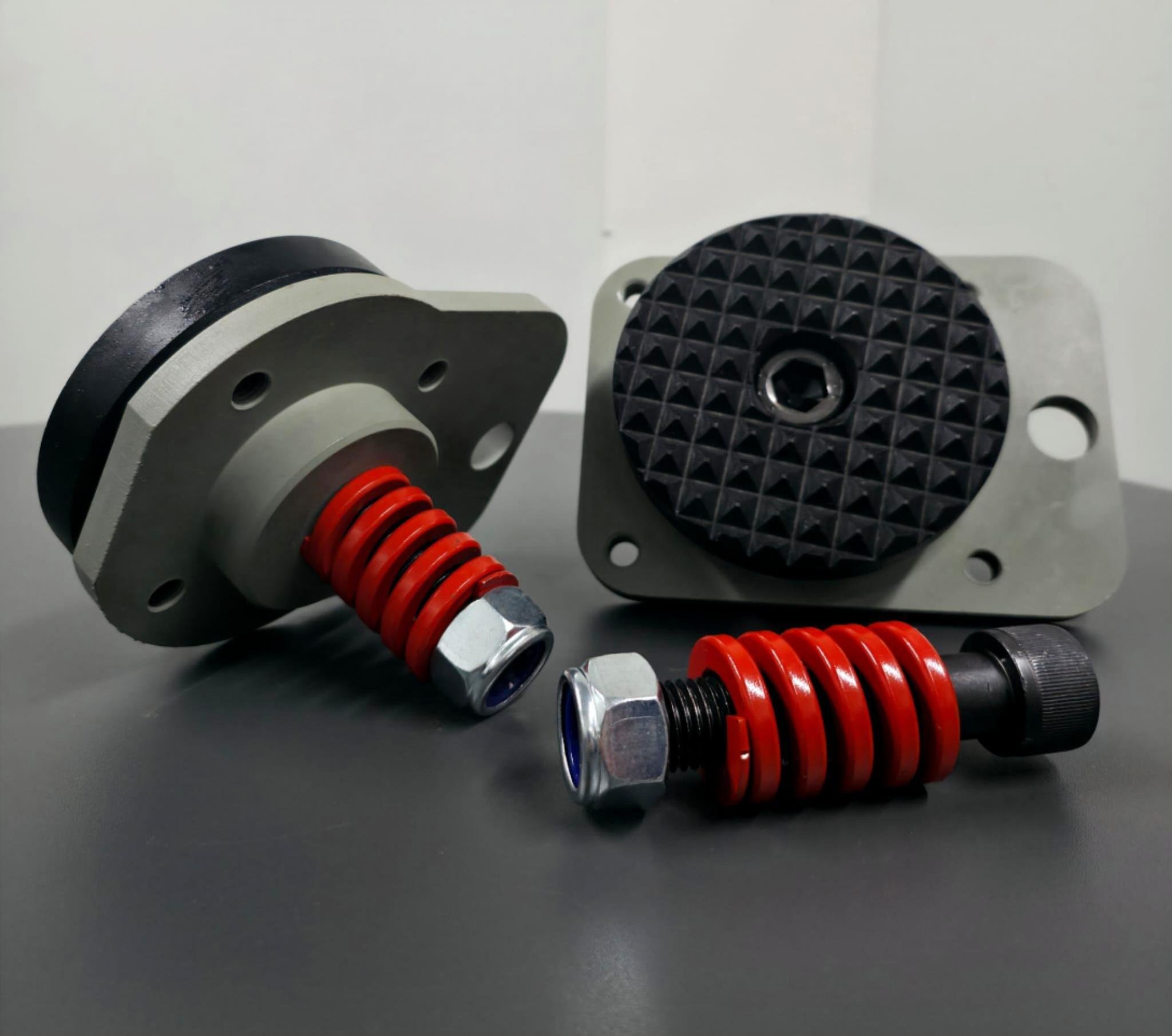 Two mechanical components with red springs and black and silver hardware, placed on a gray surface with a plain background.
