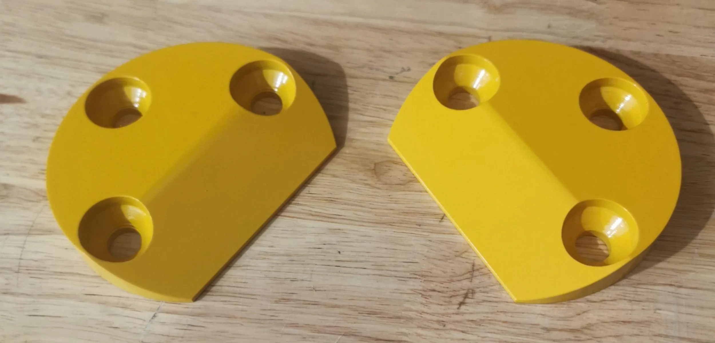 Two yellow semicircular plastic pieces with four circular holes on a wooden surface.