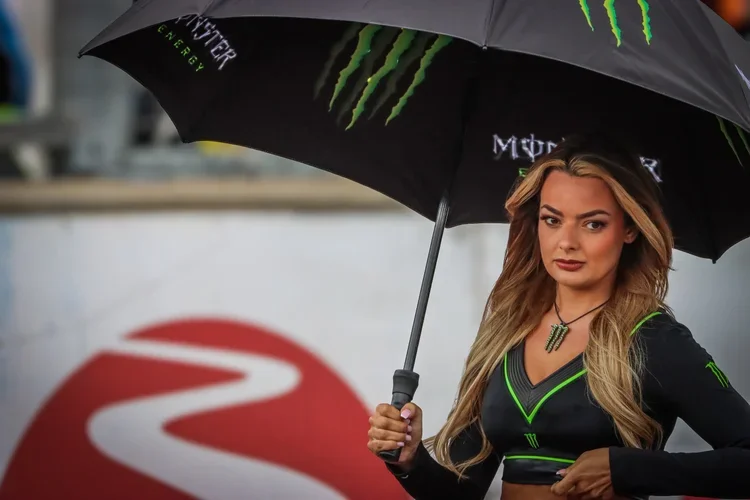 A woman holding a Monster Energy umbrella at a racing event.