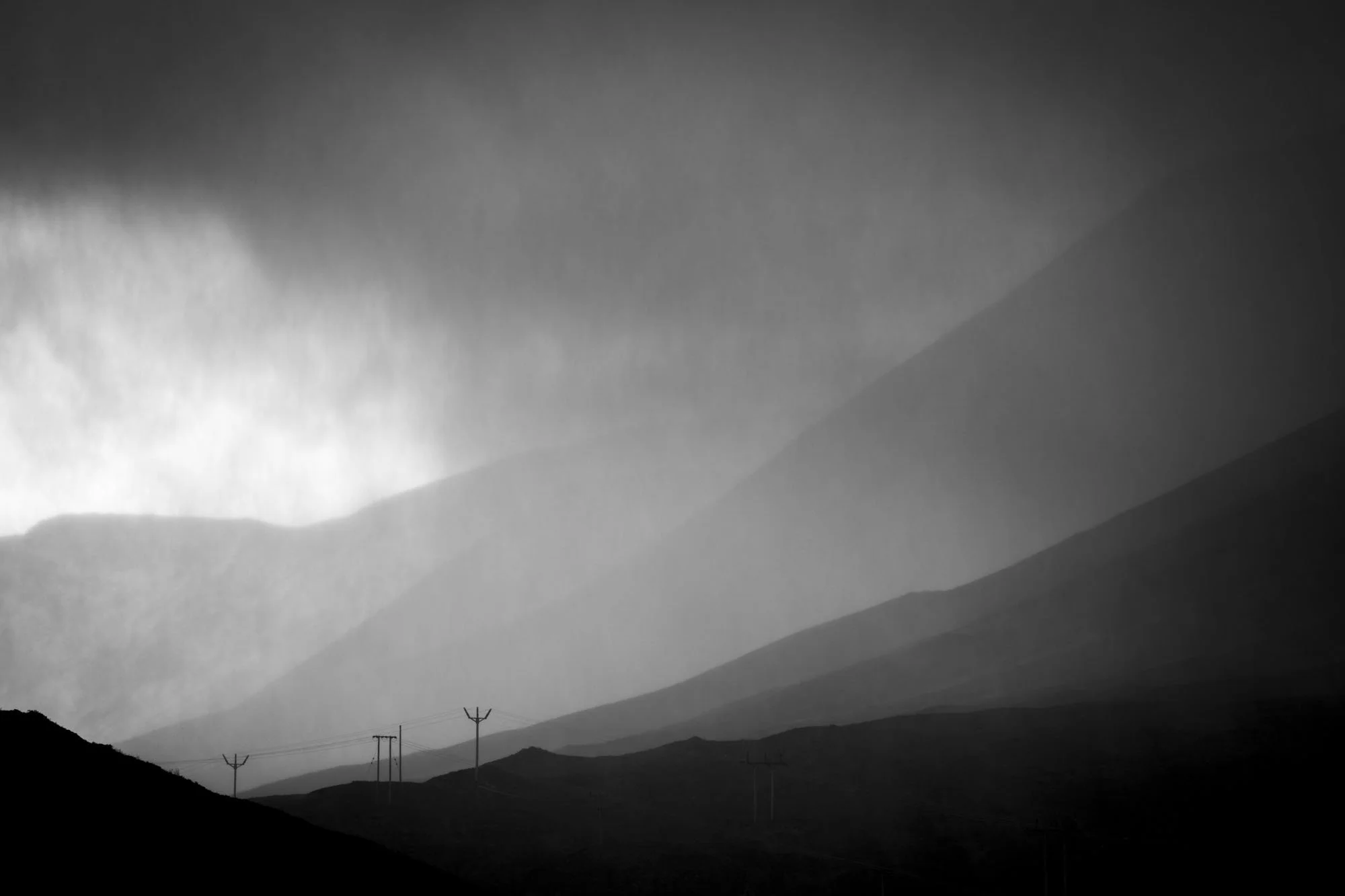 Immense weather blows across the Isle of Skye, with small power poles in the distance for scale. Photographed in black and white by Andrew Tobin for the book "Glas".
