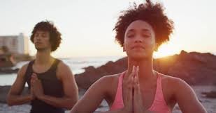 Two people practicing yoga outdoors at sunrise, focusing on meditation with hands in prayer position.