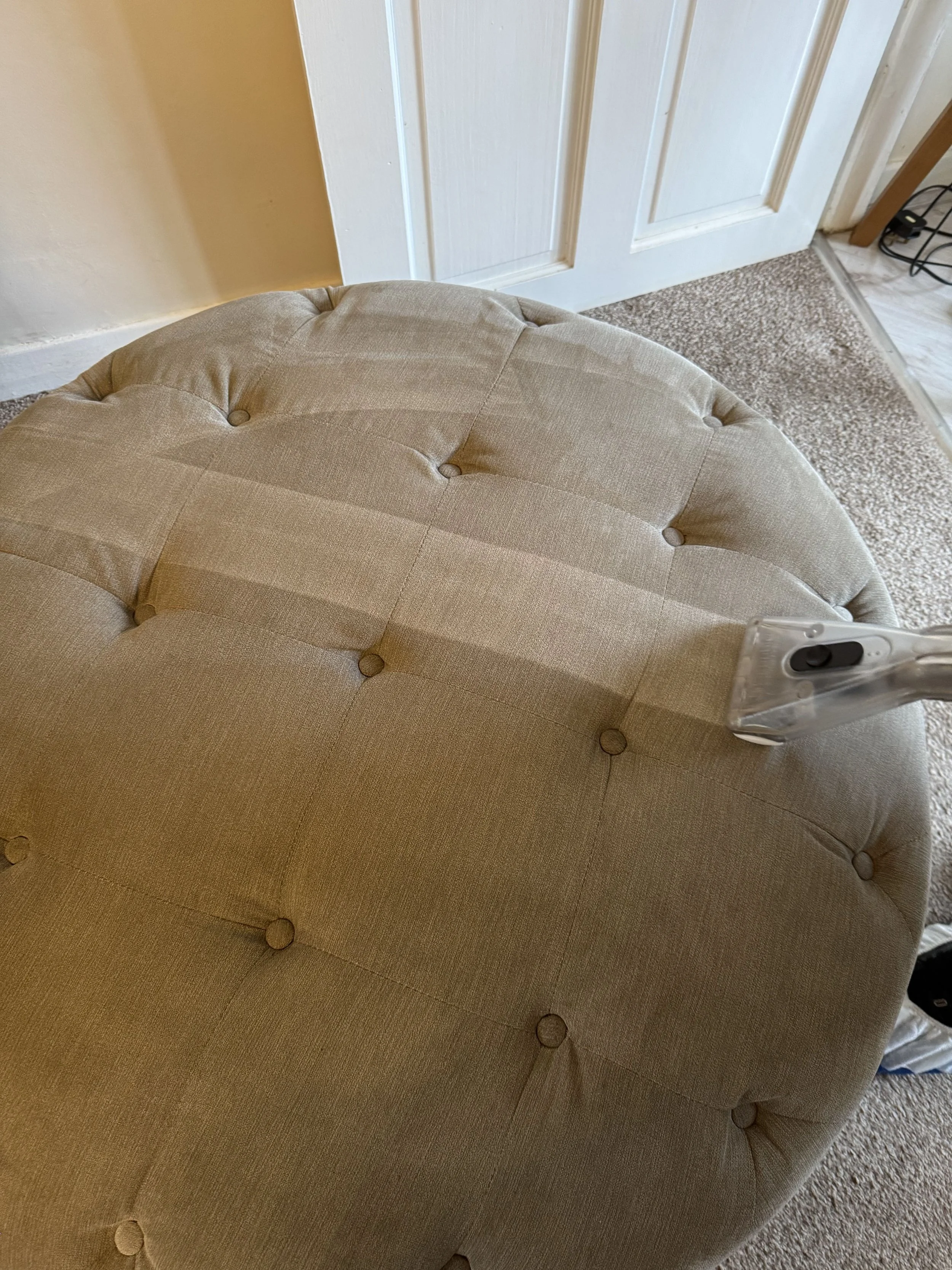 Upholstery cleaning tool cutting through built-up dirt on a fabric foot stool in Preston