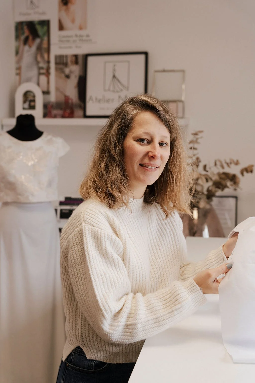 Femme préparant une robe de mariage dans une pièce lumineuse.