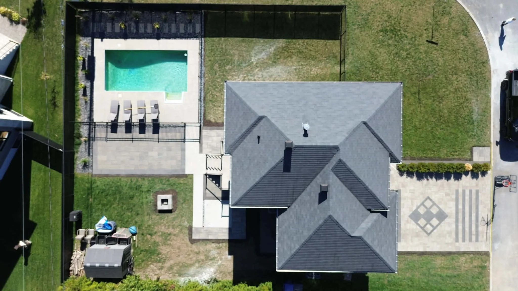 Vue aérienne d'une maison avec un toit en ardoise, un jardin, une piscine, un espace détente avec chaises longues, et une allée pavée.