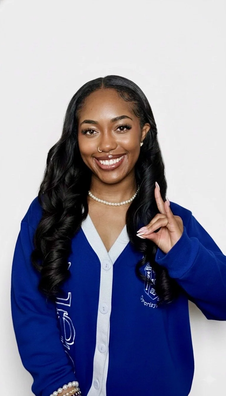 A young woman with long black hair, wearing a blue jacket with white accents, a pearl necklace, and a smile, standing against a plain white background.