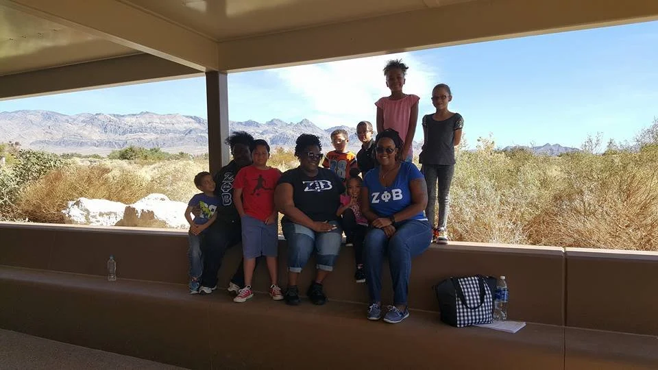 Group of nine children and two adults posing for a photo on a ledge with a desert landscape and mountains in the background.