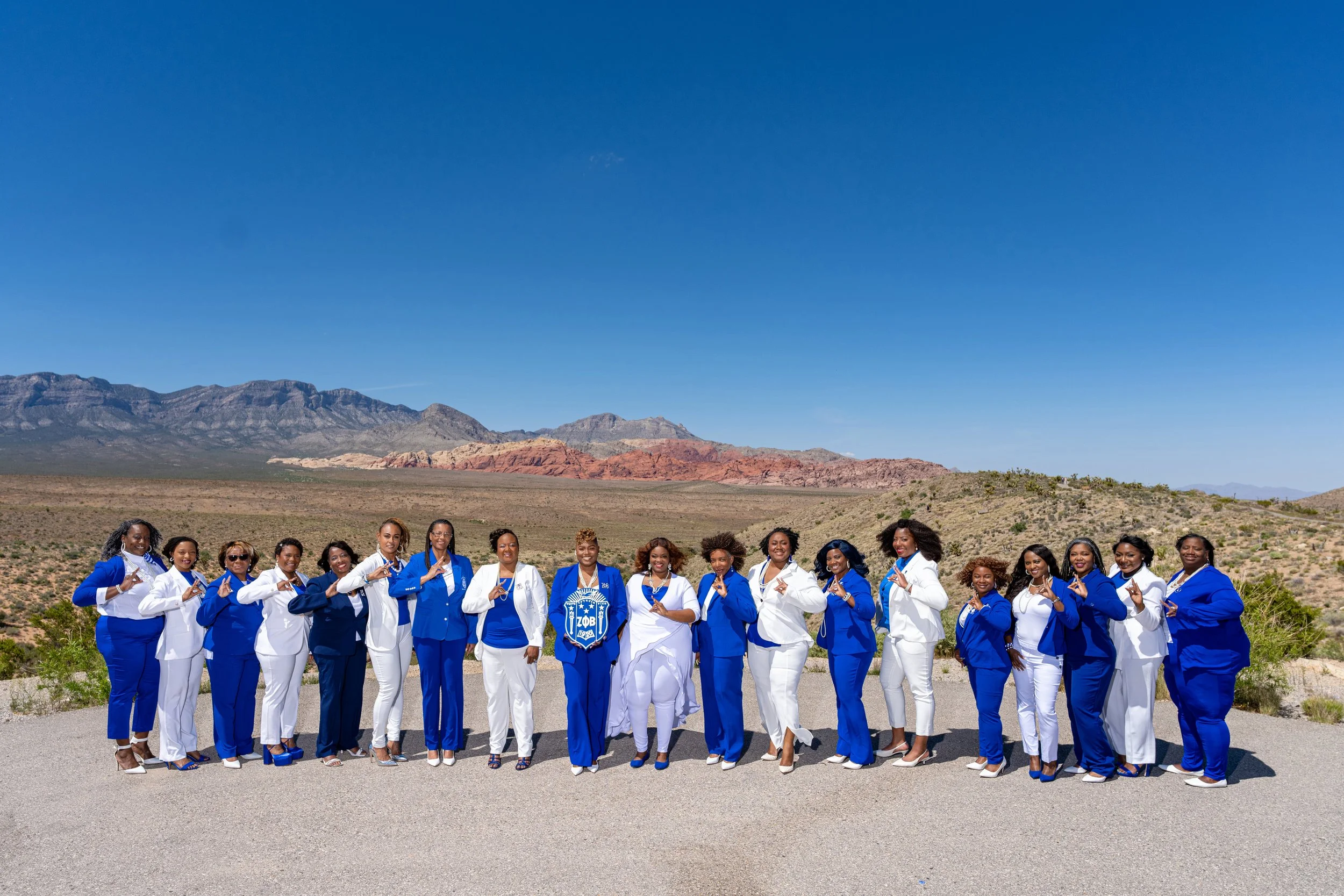 A group of women in blue and white outfits standing outdoors in a desert landscape with mountains in the background.
