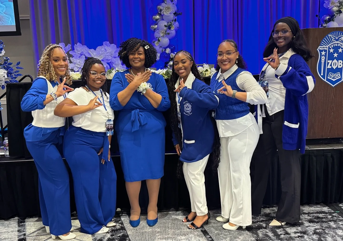 Group of women wearing blue and white outfits at a sorority event, with decorations and a podium in the background.