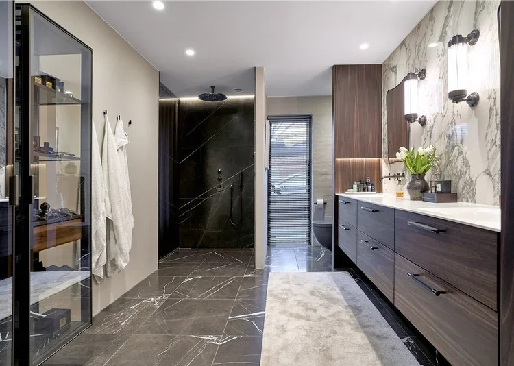 Moderne badeværelse med sort marmerflisegulv, separat bruseområde med sorte vægge, hvid vask med træskabe, vægdekoration i marmor, spejle og belysning, vindue med persienne, toilet og vask.