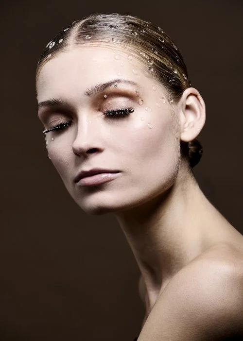 Næsen af en kvindelig model med vanddråber i et tæt close-up. Model har makeup med sølvfarvet øjenskygge og lang, sort eyeliner.