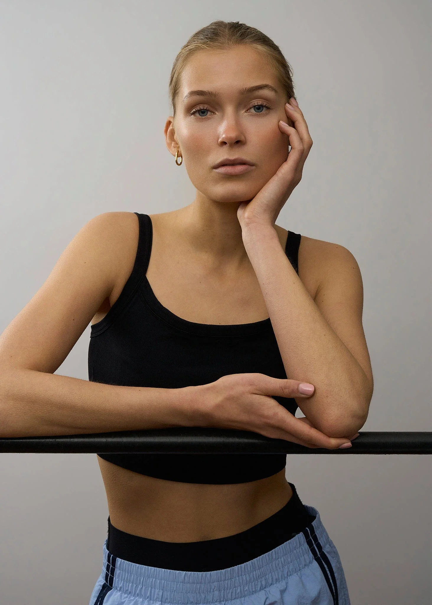 Sort-hvid portrætfotografi af en ung kvinde med langærmet sort top og grå bukser, der står foran en ensfarvet baggrund. Model. Asta Sloth Nielsen. Scoop Models. Fotograf Pia Bloch