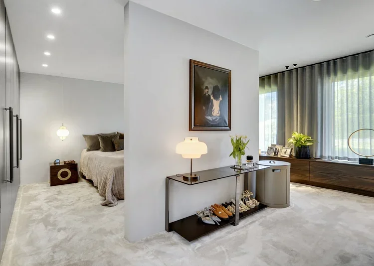 Elegant stue med sofagrupper, stort vindue med mørke gardiner, moderne interiør, kunst på væggen, plante og sko på hylde.