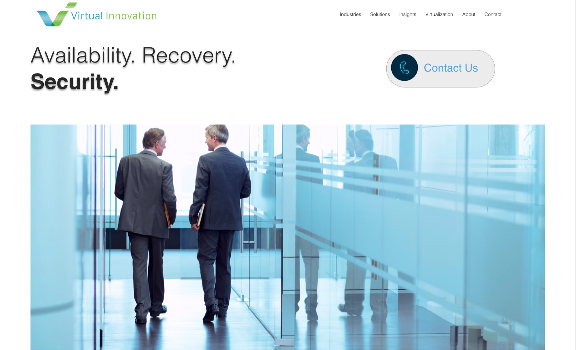 Two businessmen in suits walking and talking in a modern office corridor with glass walls and reflections.