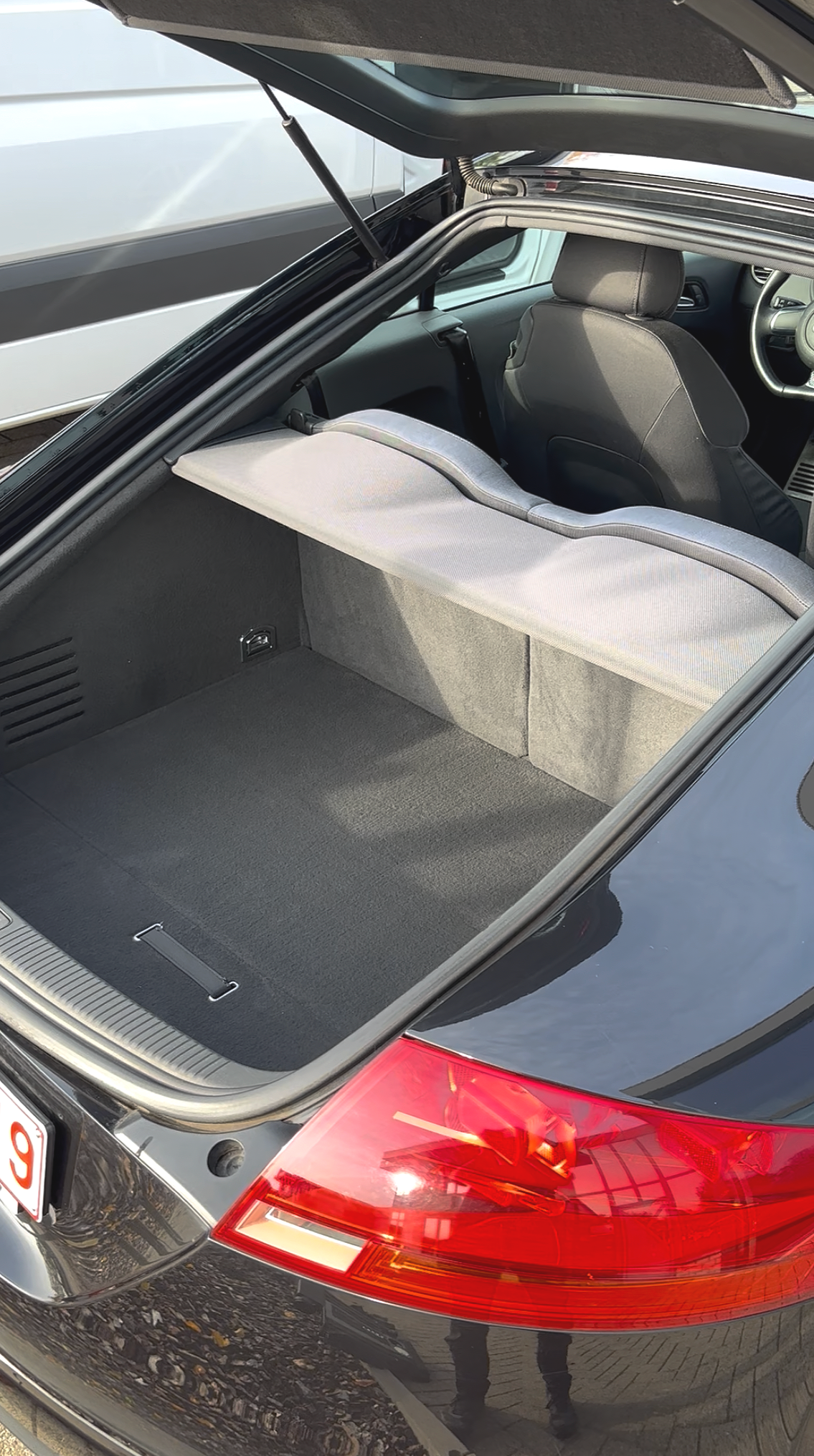 De foto toont de open achterklep van een zwarte auto, waarbij de lege kofferbak te zien is. In de achtergrond is de voorkant van de auto met het dashboard en de bestuurdersstoel zichtbaar.